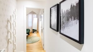 Un couloir avec deux tableaux encadrés accrochés au mur, une porte donnant sur une pièce avec un lit et une chaise, et un mur à motifs sur le côté gauche.