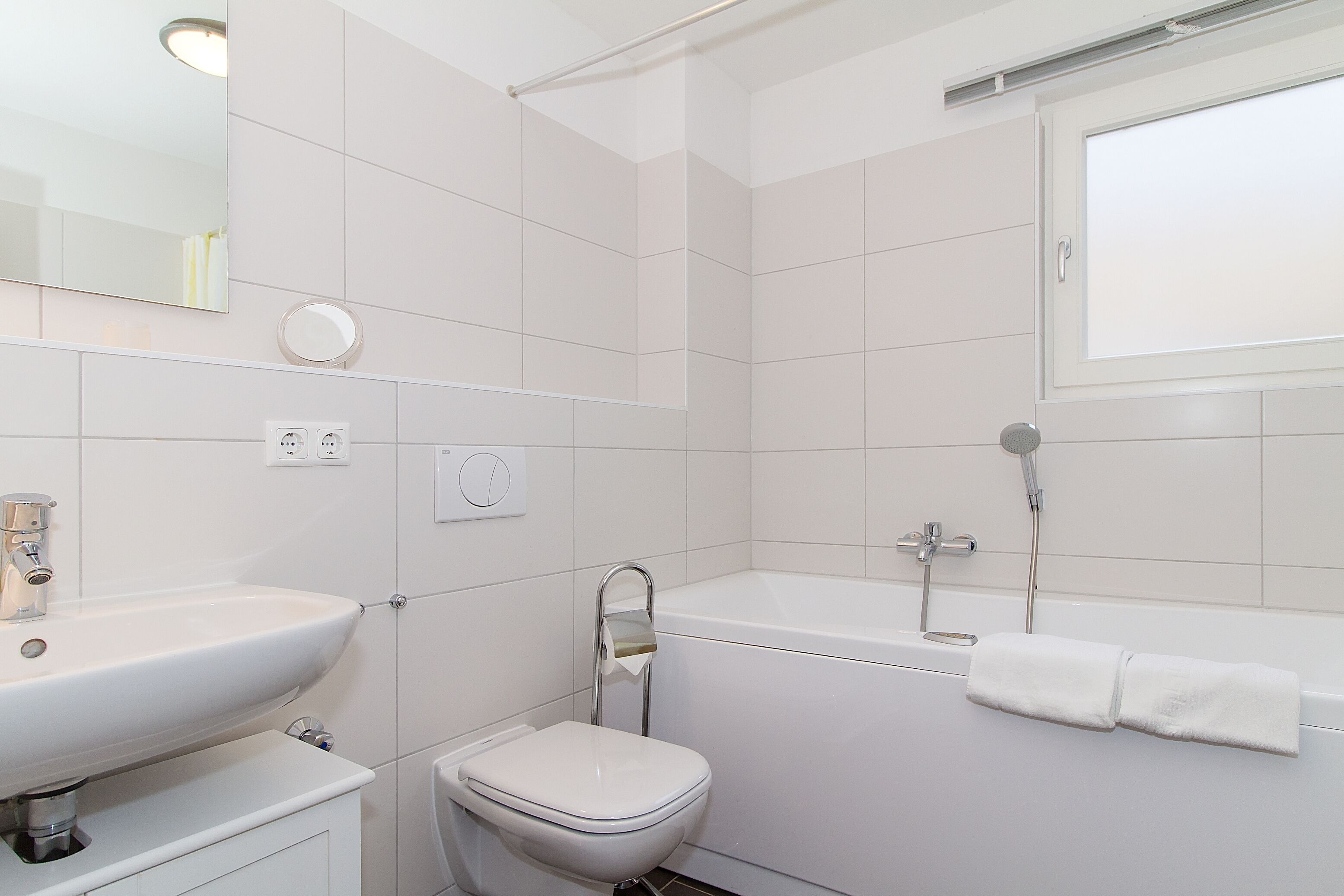 Ein modernes Badezimmer mit Waschbecken, Toilette und Badewanne in Weiß.