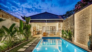 A swimming pool with a tiled deck, surrounded by plants and a stone wall with inscriptions.