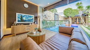 A modern living room with a large flat-screen TV, a wooden console, a glass coffee table, and a leather sofa.