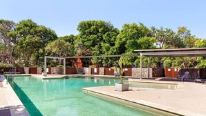 A swimming pool with a covered area and lounge chairs, surrounded by trees and stone walls. - Twin Waters Seaside Resort Life (Twin Waters)