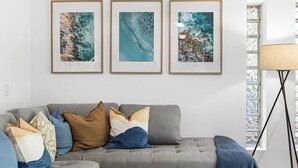 A living room with a grey sofa, multiple cushions, and three framed abstract paintings on the wall. - Twin Waters Seaside Resort Life (Twin Waters)
