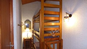 A wooden staircase with a unique antler design at the bottom, a small table with a lamp, and a wall-mounted light fixture.