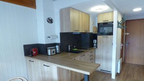 A compact kitchen with wooden cabinets, a built-in oven, and a coffee machine.