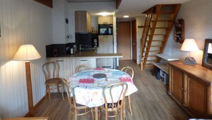 A compact kitchen with wooden cabinets, a dining table with chairs, and a staircase leading to an upper level.