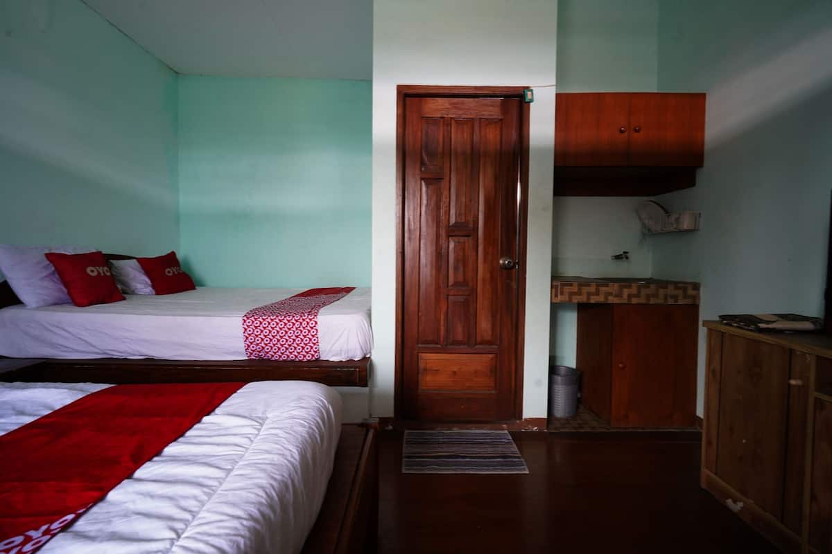 A room with two beds, a wooden wardrobe, and a small kitchenette.