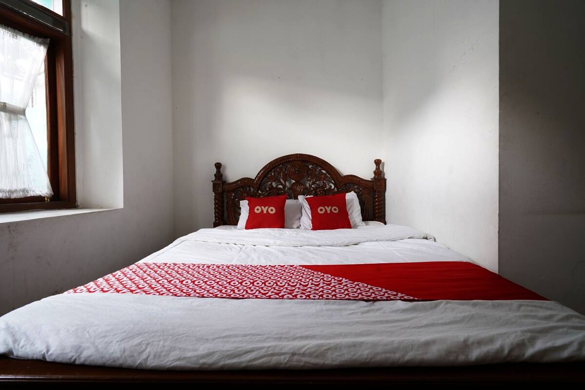 A bed with a wooden headboard, white bedding, and two red pillows with "OYO" text.