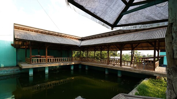 A covered outdoor area with a wooden deck over water, supported by pillars, and a metal roof structure. - OYO 93248 Villa Syariah Astuti Lestari (Parongpong)