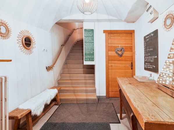 A wooden staircase leading to a room with a heart-shaped decoration on the door, a bench, a table, and a wall with a mirror and a sign.