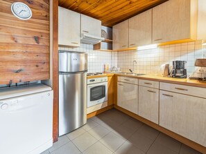 A kitchen with wooden cabinets, a stainless steel refrigerator, an oven, a sink, and a coffee maker. - Cozy 1BR+Alcove in Serre Chevalier with Pool, WiFi, Private Parking, Near Slopes (Saint-Chaffrey)