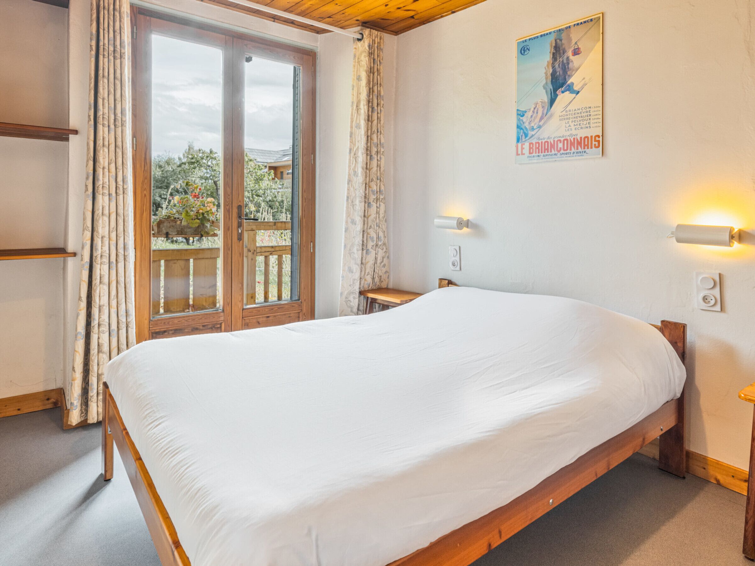 Un dormitorio con una cama de madera, una ventana con cortinas, un cartel en la pared y una mesita.