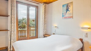 Une chambre avec un lit en bois, une fenêtre avec des rideaux, une affiche accrochée au mur et une petite table.