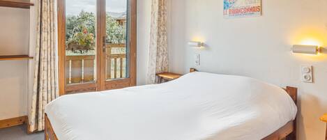 Un dormitorio con una cama de madera, una ventana con cortinas, un cartel en la pared y una mesita.