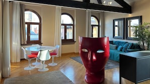 A modern interior with exposed wooden beams, a round dining table with white chairs, a red sculptural piece, and a teal sofa. - Piazza Erbe Lodge (Verona)