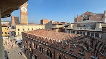 Un edificio histórico con ventanas de arco y tejado de tejas, parte de una zona urbana más amplia con una torre del reloj.