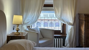 A hotel room with a bed, a chair, a lamp, and a view of the outside balcony. - Piazza Erbe Lodge (Verona)