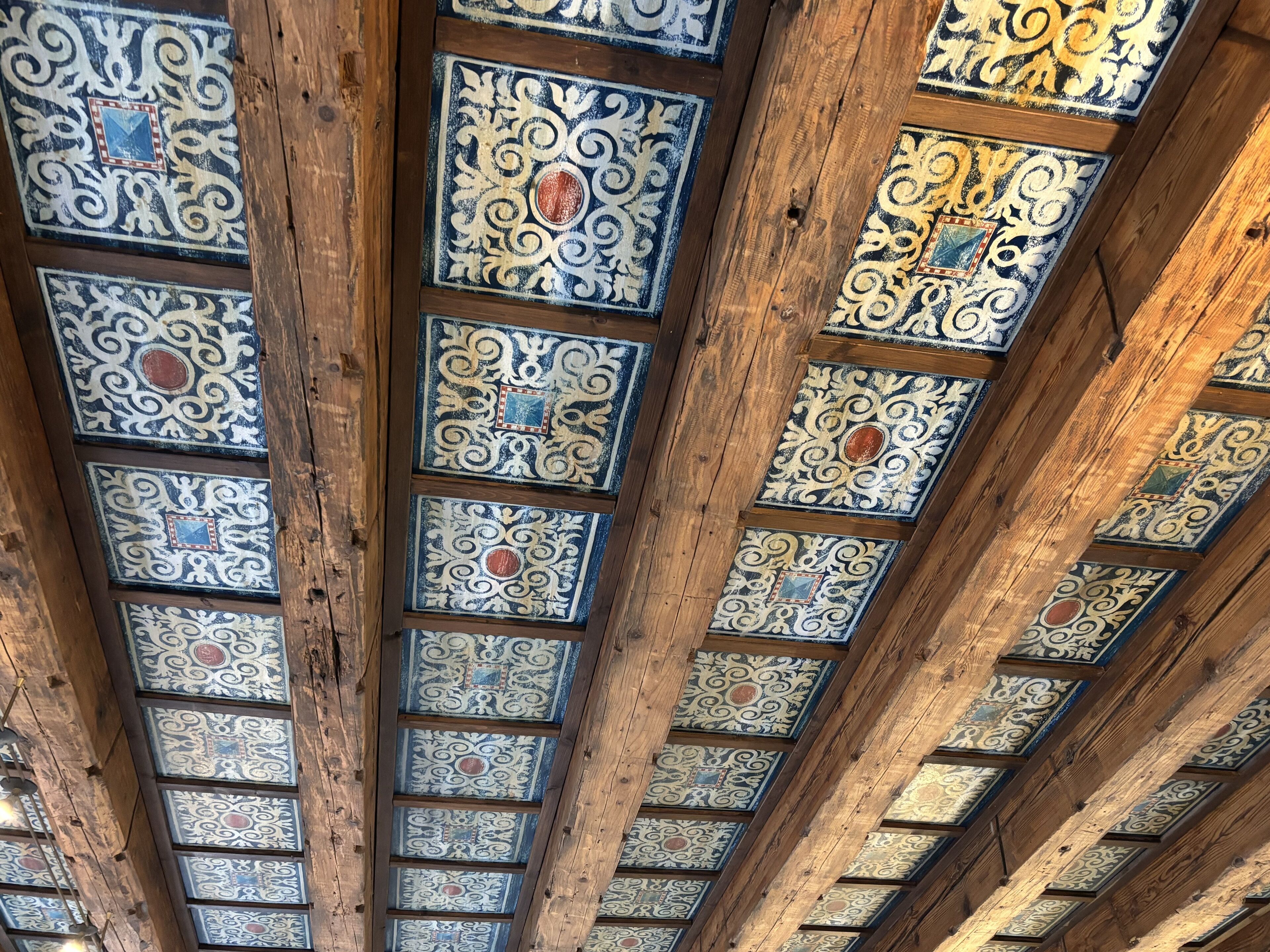 A ceiling with intricate tile patterns and wooden beams.