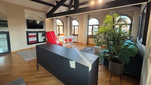 A spacious living room with a modern design, featuring a large black sofa, a dining area with a white table and red chairs, and a large potted plant. - Piazza Erbe Lodge (Verona)