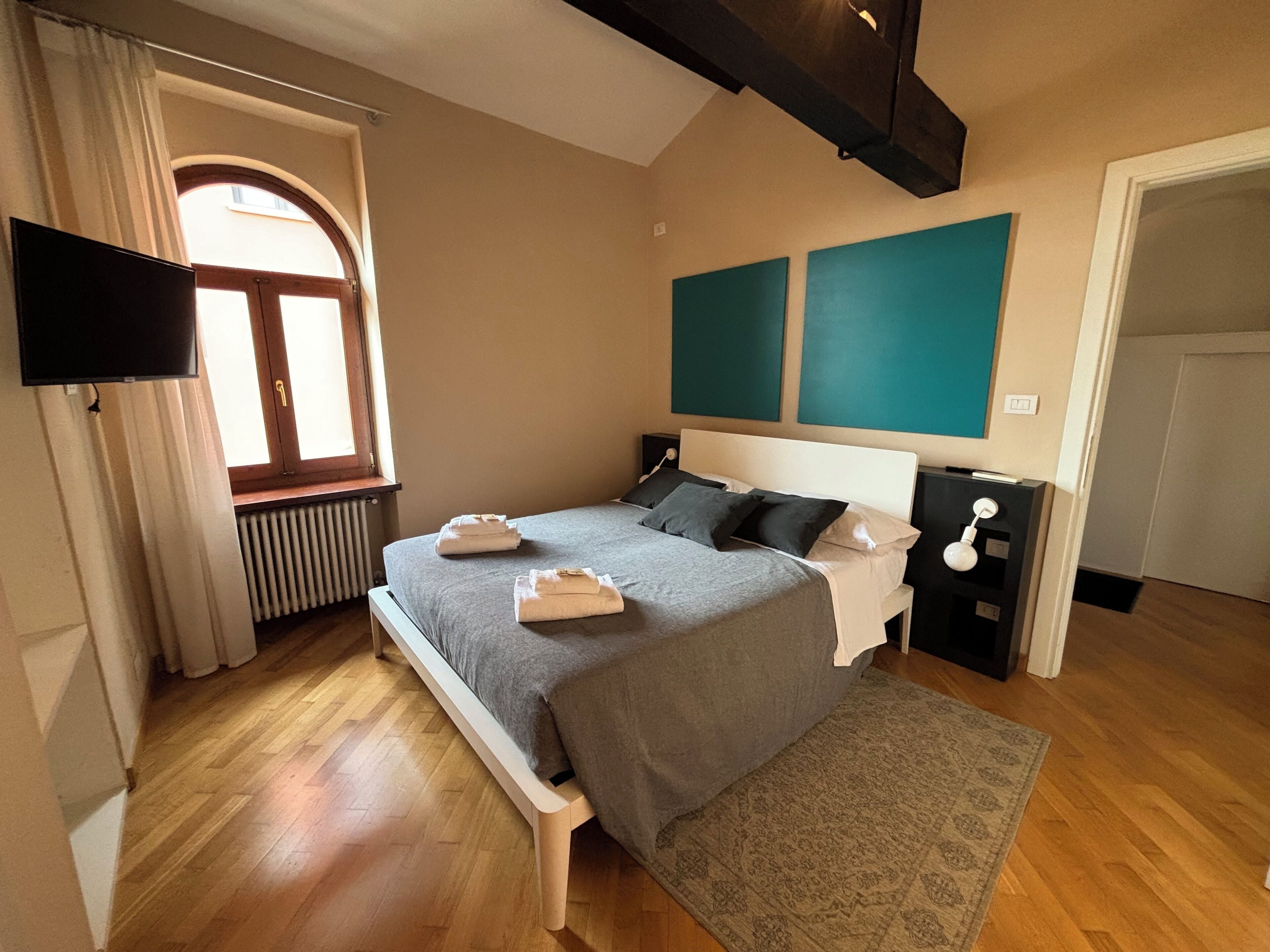 A bedroom with a bed, bedside tables, a TV, a window, and a radiator.