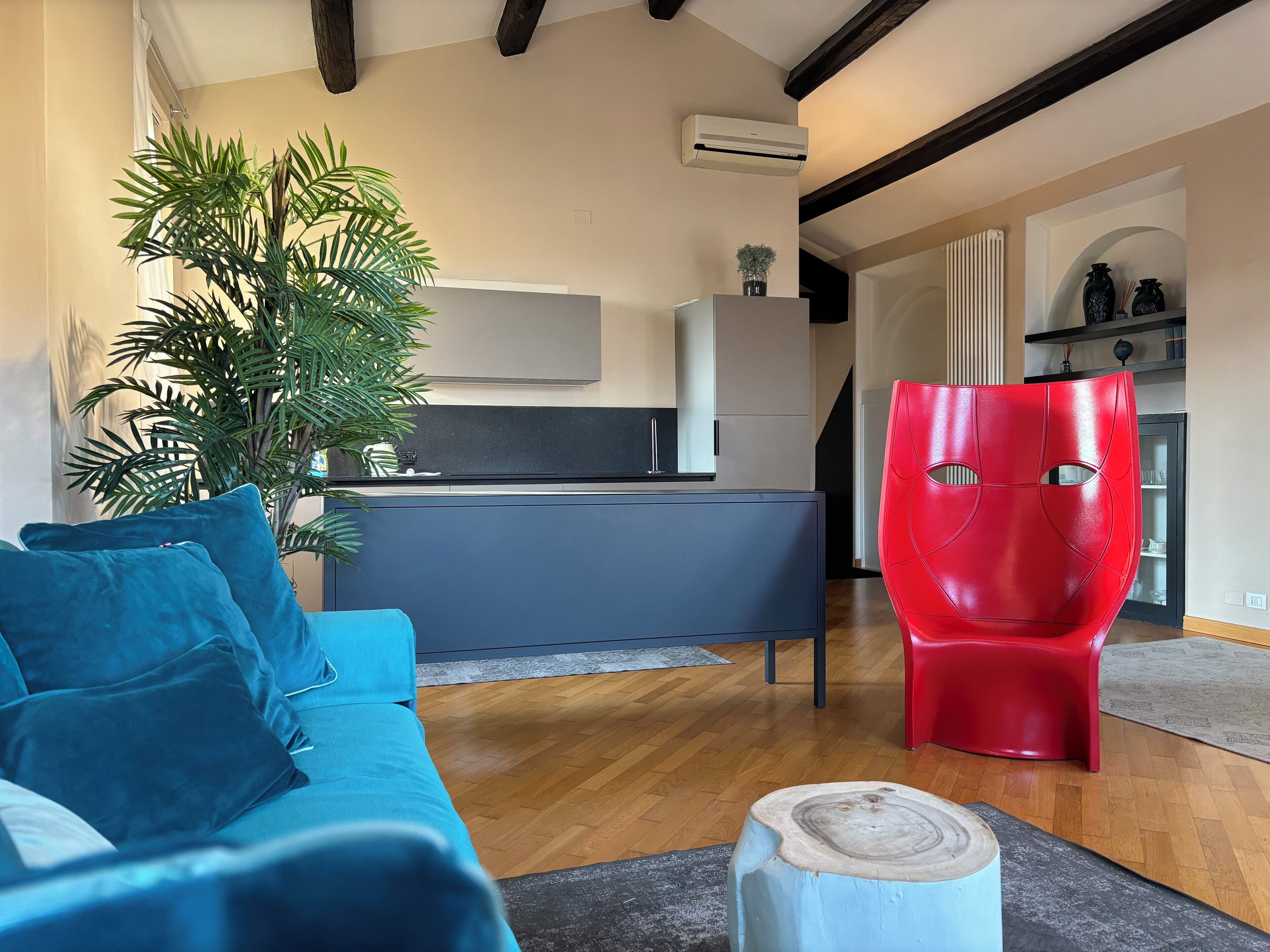 Uma sala de estar moderna com um sofá azul, uma poltrona vermelha, uma mesa de centro de madeira e uma planta grande.