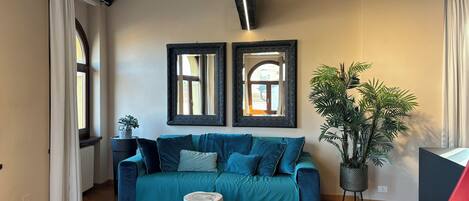 Una sala de estar con un sofá color turquesa, dos espejos en la pared, una planta en maceta y un radiador.