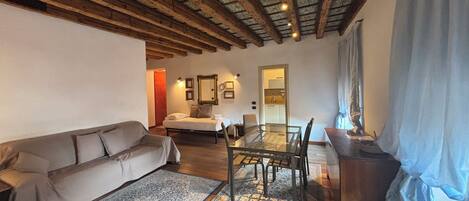A cozy living room with a sofa, a dining table with chairs, a patterned rug, and a wooden ceiling.