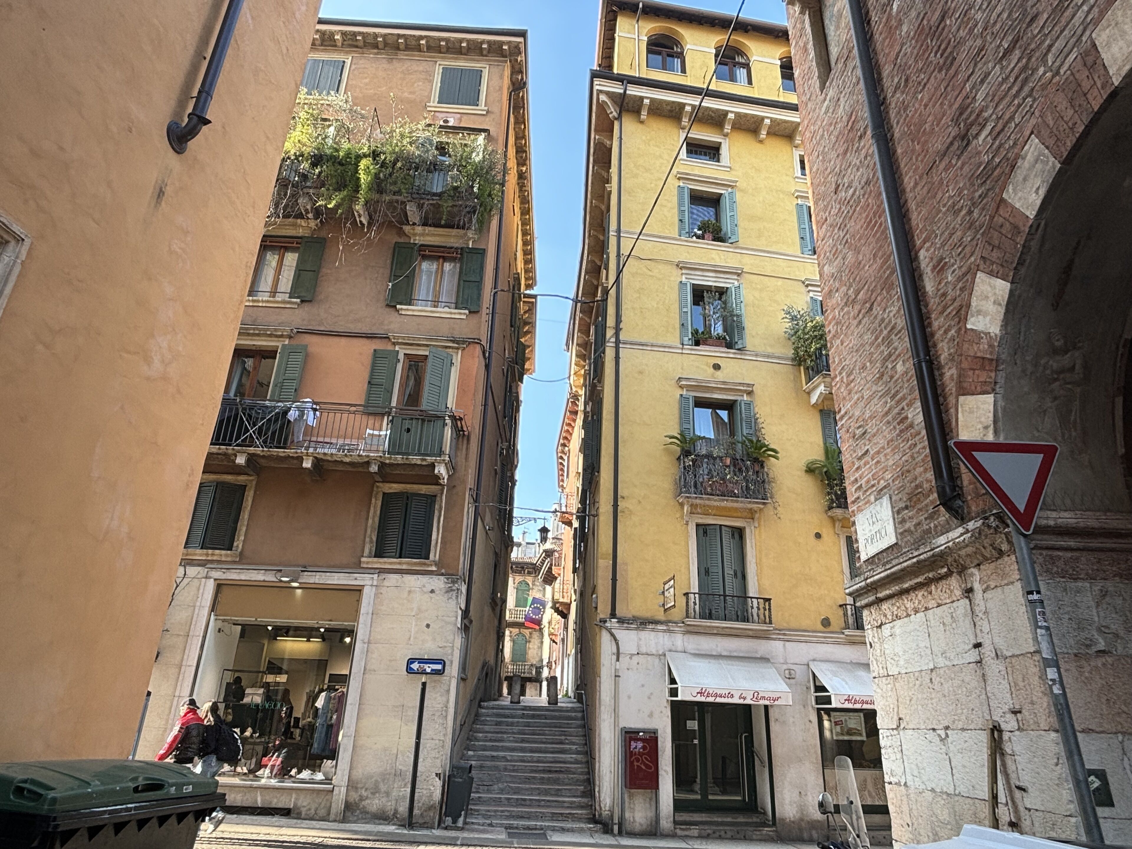 A narrow street with multi-story buildings, a visible shop entrance, and a pedestrian crossing.