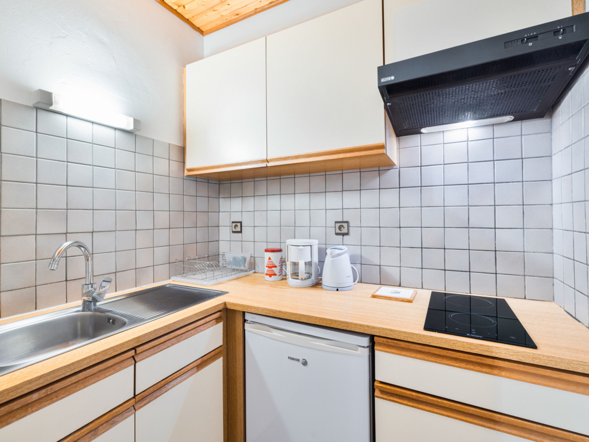 Eine moderne Küche mit weißen Schränken, einer Edelstahl-Spüle, einer Kaffeemaschine und einem eingebauten Backofen.