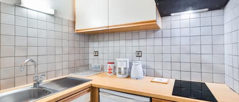 Una cocina moderna con armarios blancos, un lavamanos de acero inoxidable, una cafetera y un horno empotrado.