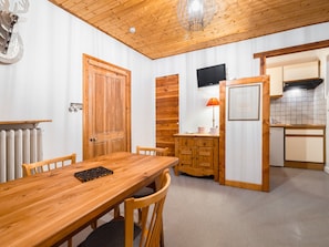 A wooden dining table with chairs, a kitchen area with a stove, and a television mounted on the wall.