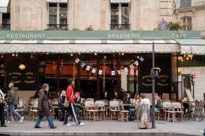 An outdoor cafe with tables and chairs, a sign above indicating it's a restaurant, and a street scene with people walking by. - Sunrise Synergy, by Veeve (Paris)