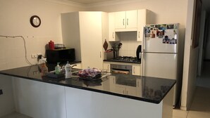 Keittiössä on valkoiset kaapit, musta työtaso, mikroaaltouuni, liesi ja jääkaappi, jonka oveen on kiinnitetty valokuvia.