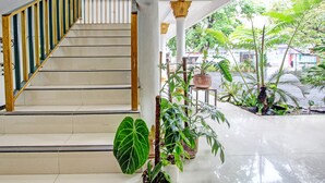 A staircase with a wooden handrail and beige steps, leading to a covered area with potted plants and a view of the outside.
