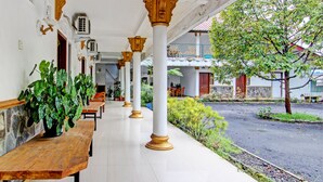 A covered outdoor area with wooden benches, potted plants, and a tiled floor.
