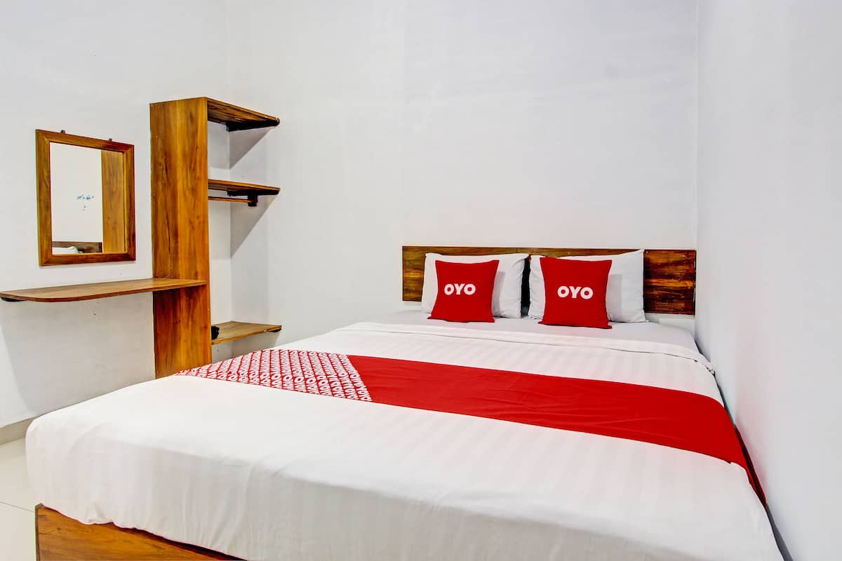 Un lit bien fait, recouvert d’une couverture rouge et blanche, avec deux oreillers sur lesquels est inscrit le mot « OYO », et une tête de lit en bois.