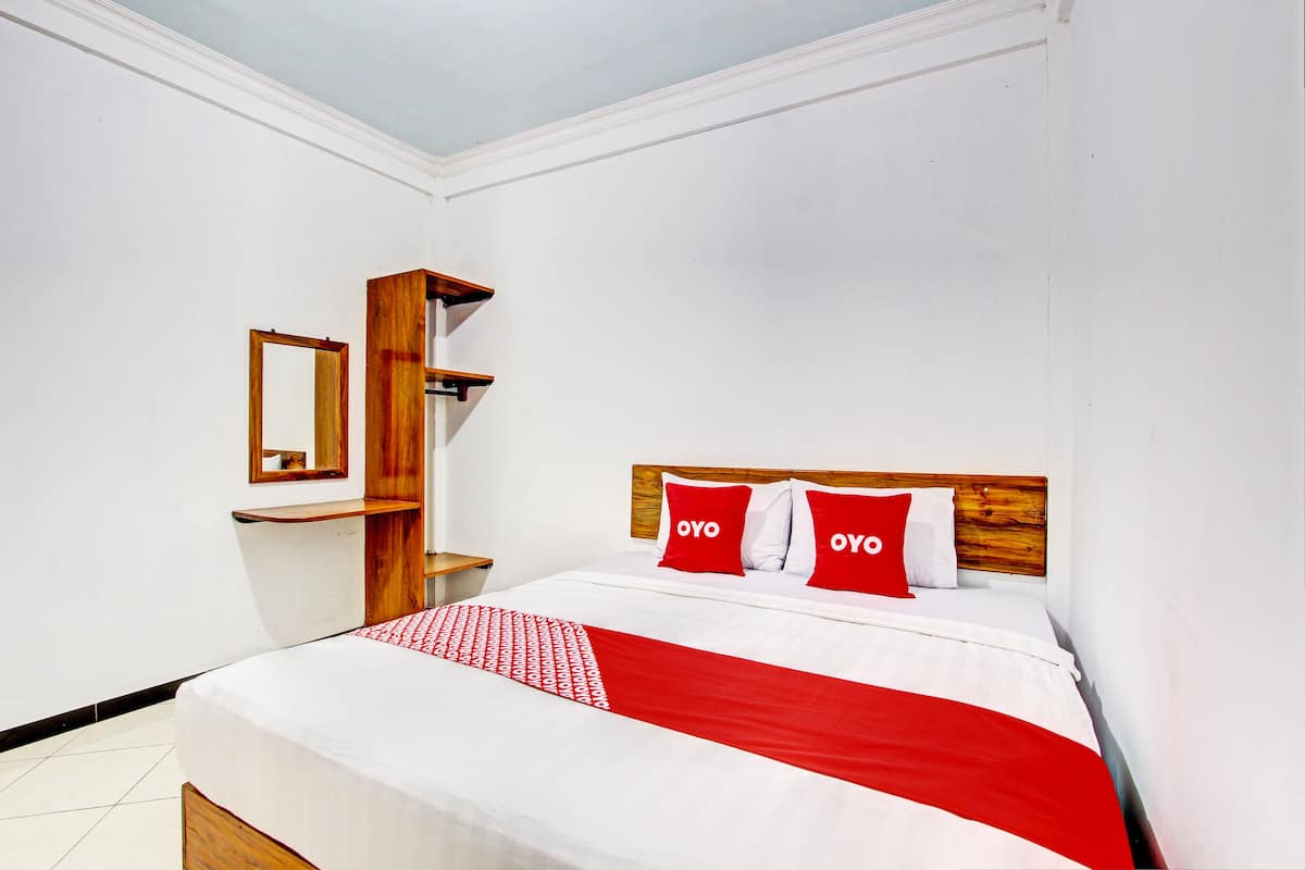 Un lit bien fait, recouvert d’une couverture rouge et blanche, avec deux oreillers sur lesquels est inscrit le mot « OYO », et une tête de lit en bois.
