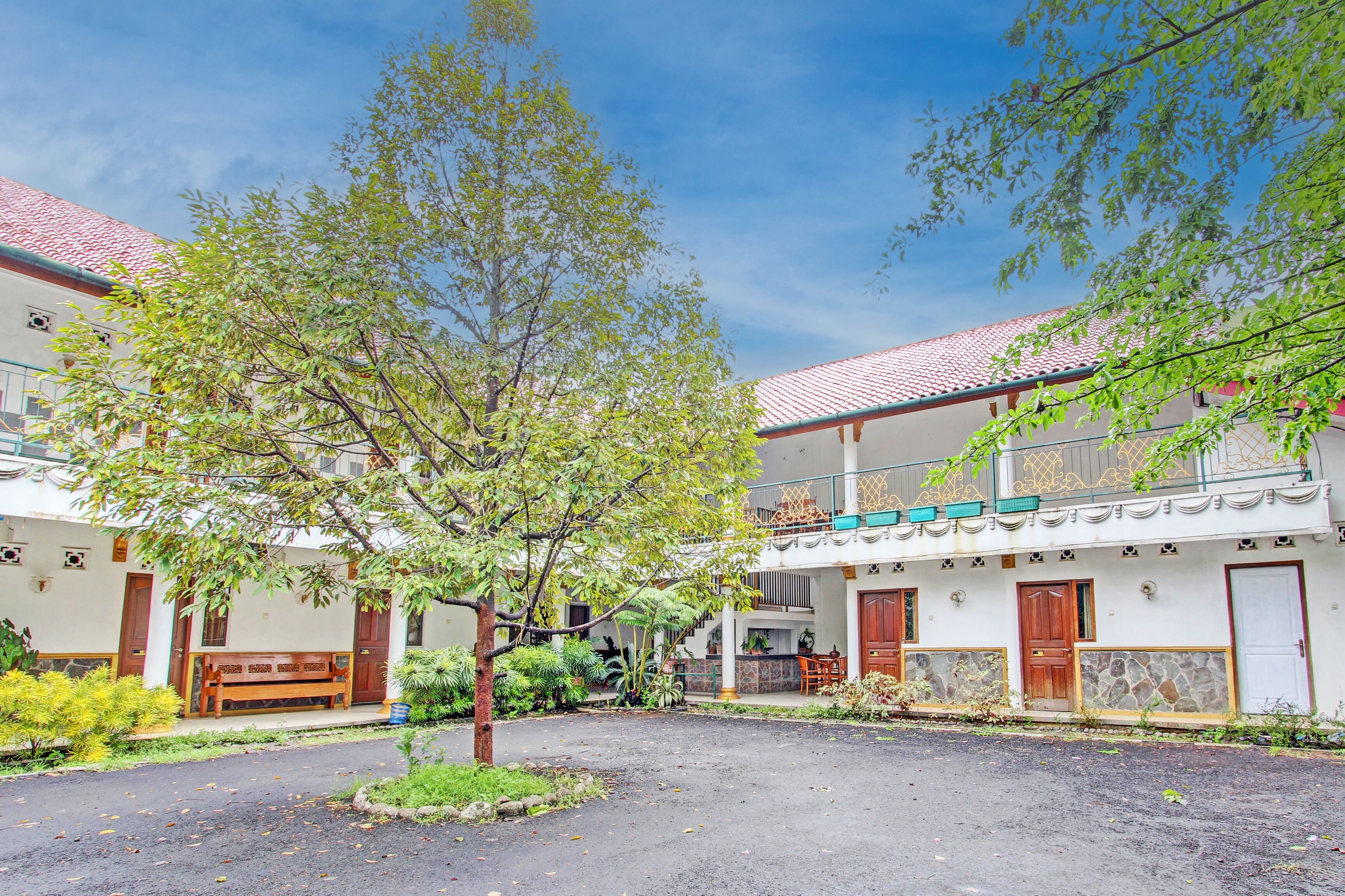 Un patio con un árbol, un banco y un edificio de techo con tejas y balcones.