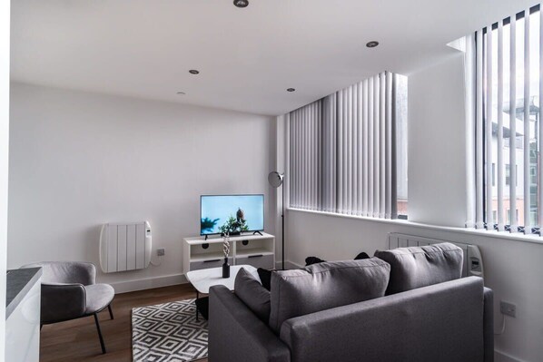 A modern living room with a grey sofa, a white coffee table, and a TV on a white stand.