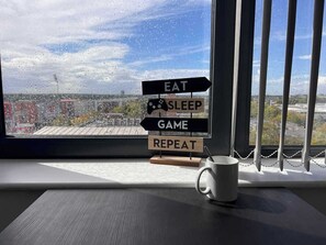 A window with a view of a cityscape, a sign with words 'EAT', 'SLEEP', 'GAME', 'REPEAT', and a white mug on a windowsill.