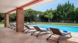 Un espace extérieur abrité comprenant une piscine, des chaises longues et une vue sur les arbres et la pelouse.