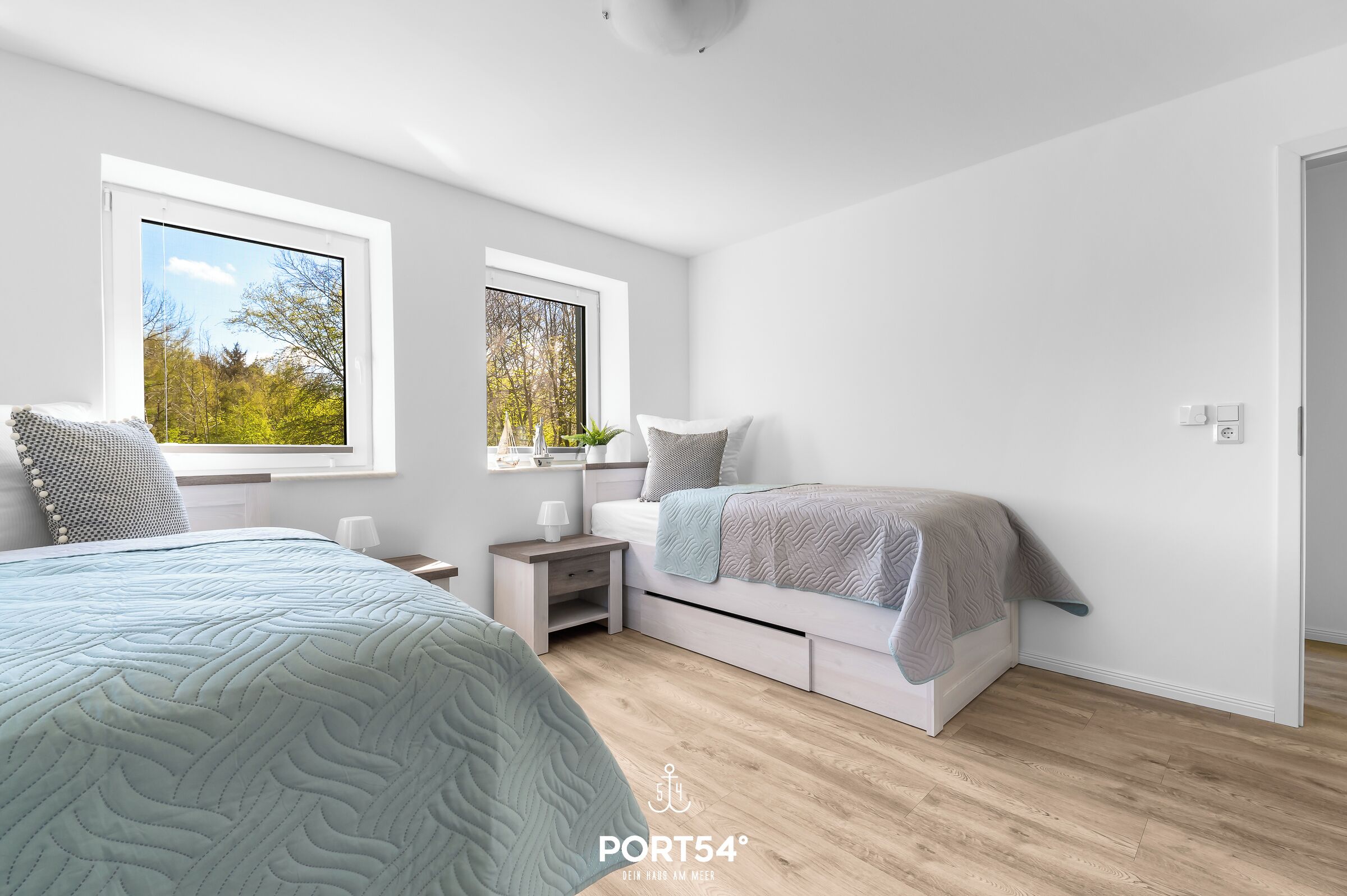 A modern bedroom with two beds, a nightstand, and a window with a view of trees.