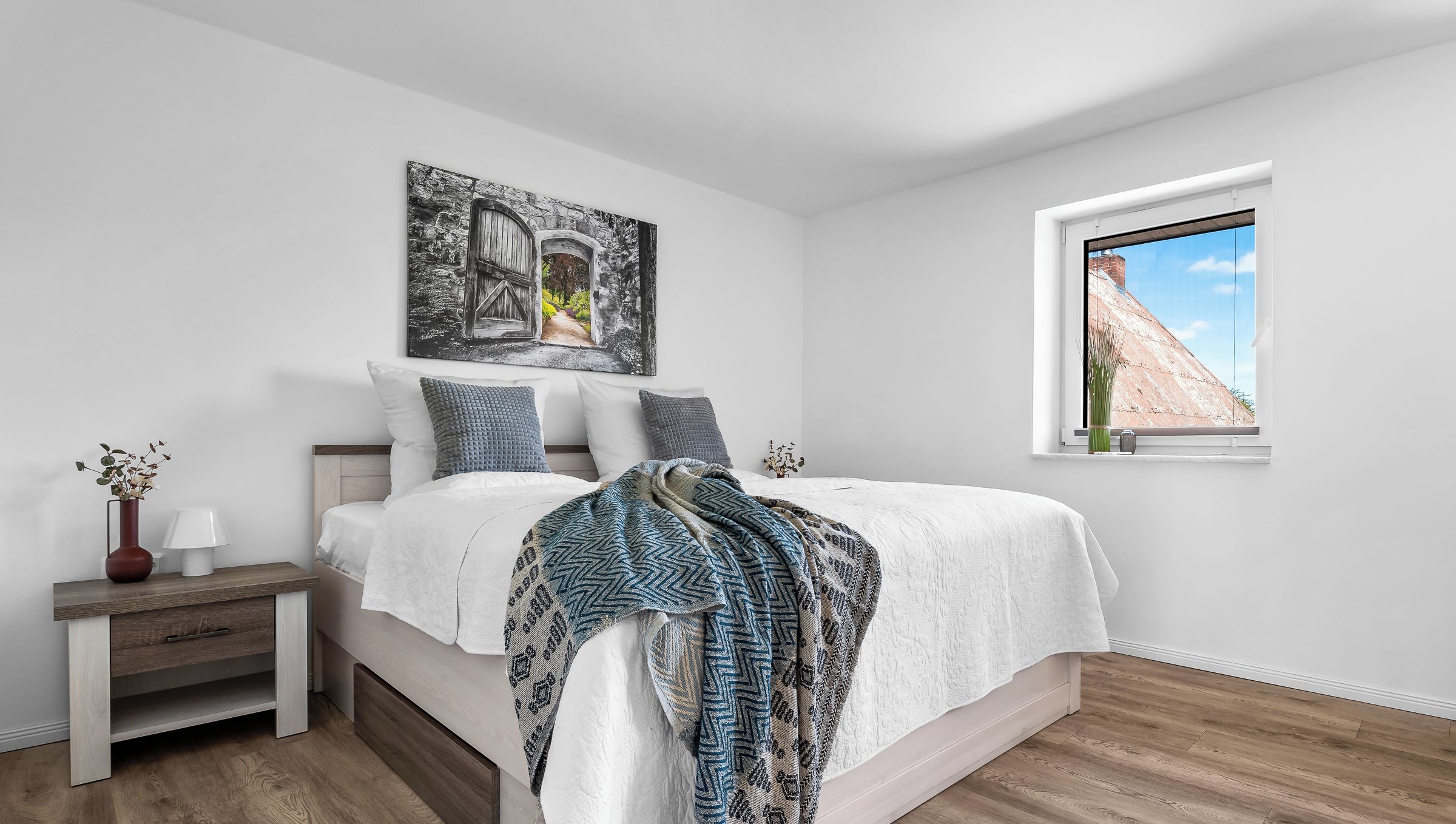 Ein Schlafzimmer mit Bett, Nachttisch, Fenster und einem Bild an der Wand.