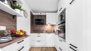 Uma cozinha moderna com armários brancos, bancada de madeira e diversos eletrodomésticos, incluindo micro-ondas e forno.