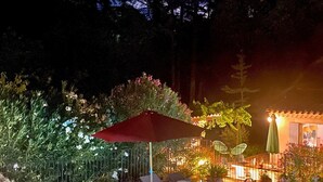 A nighttime outdoor pool area with lounge chairs, a red umbrella, and a building with lights in the background. - Maison Provençale Avec Grande Piscine à Goult en Plein Coeur du Luberon (Goult)