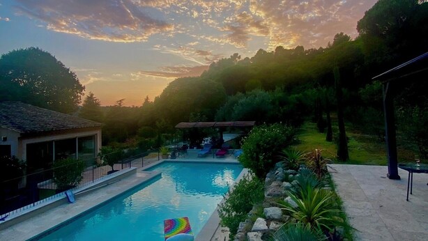 A swimming pool with lounge chairs and a rainbow-colored float, surrounded by greenery and a gazebo. - Maison Provençale Avec Grande Piscine à Goult en Plein Coeur du Luberon (Goult)