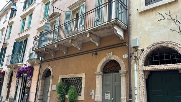 A building with a green door, a balcony with a metal railing, and a flower arrangement on the ground floor. - LOFT 17 ARENA (Verona)