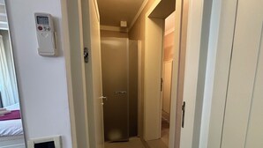 A narrow hallway with a door at the end, a thermostat on the wall, and a small vent on the floor. - LOFT 17 ARENA (Verona)