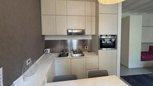 A modern kitchen with a built-in oven, a sink, and a stove. There is a dining area with a table and chairs. - LOFT 17 ARENA (Verona)