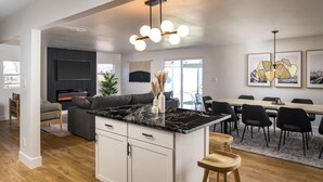 A modern kitchen with a marble countertop, a central island, and a dining area with a wooden table and chairs. - Spacious + Stylish Home w/HotTub 12min to Downtown (Westminster)