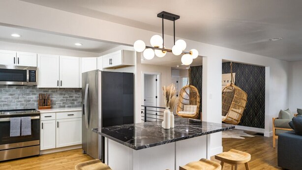 A modern kitchen with white cabinets, a black refrigerator, a marble island with stools, and a hanging light fixture. - Spacious + Stylish Home w/HotTub 12min to Downtown (Westminster)